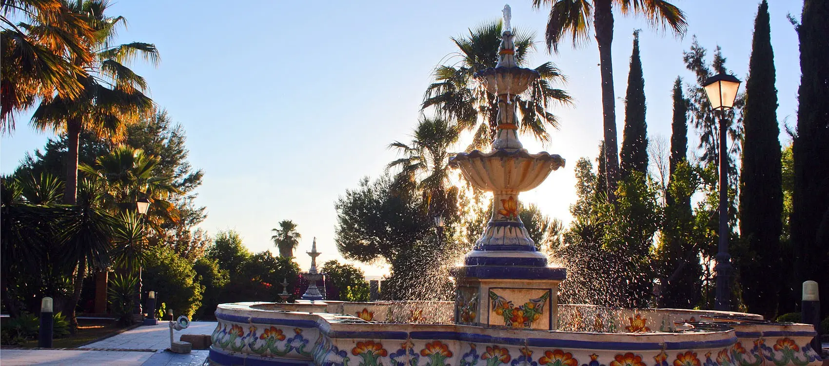 Fuente de azulejo sevillano contra el cielo de la tarde, entre palmeras